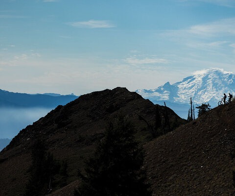 Mount Rainier dwarfs Aric Duncan and Michael Fischer as they take in the view before ripping down a golden hillside meadow.